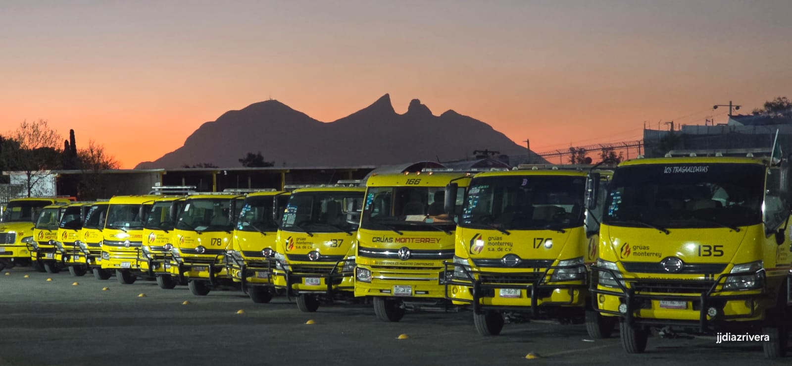 Flotilla de grúas amarillas de Grúas Monterrey alineada al atardecer, con el Cerro de la Silla al fondo.